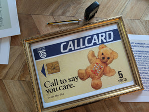 Framed Callcard advertisement with teddy bear graphic on a wooden floor.